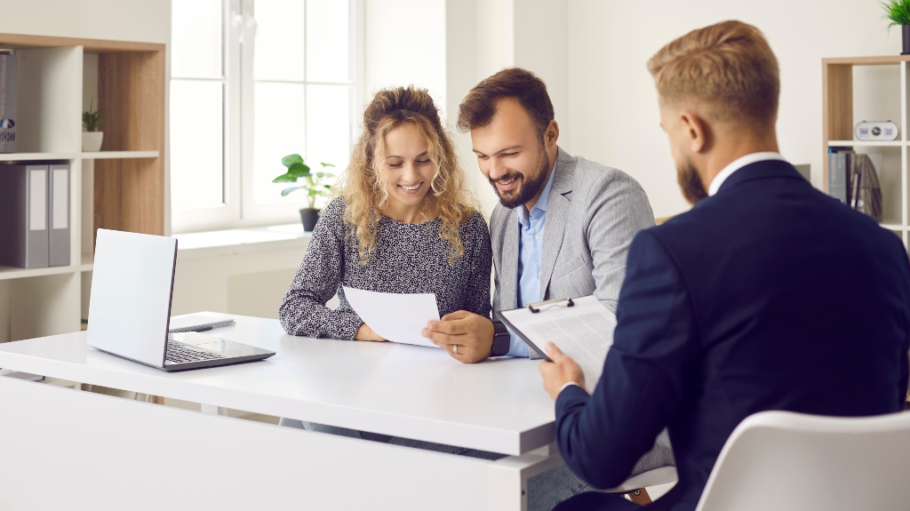 Happy couple sitting at desk in attorney's office and reading papers that he gave them