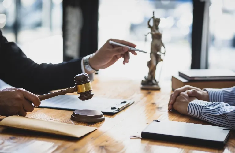 Two individuals in a legal consultation with a judge’s gavel and Lady Justice statue on a wooden table.