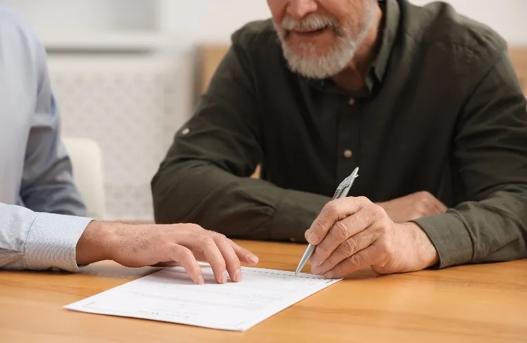 Two men reviewing and signing a document on a wooden table, one holding a pen.