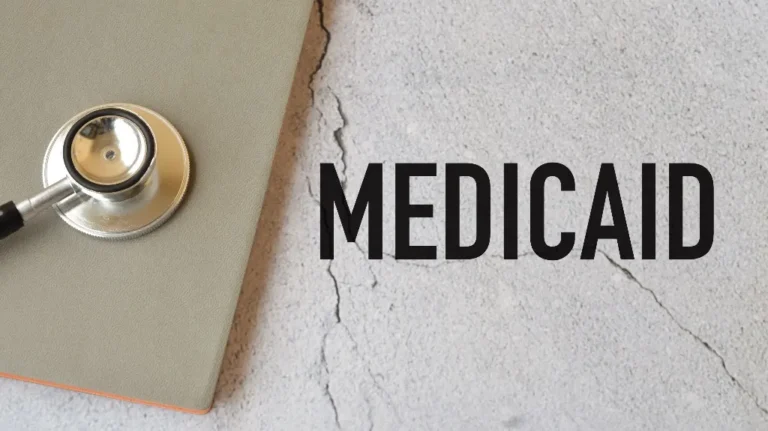 Stethoscope on closed gray folder beside the word "MEDICAID" on cracked concrete surface.