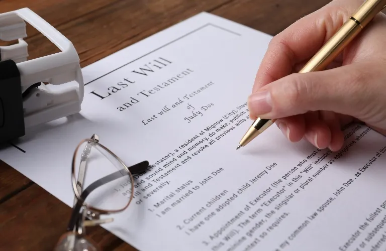 Hand holding gold pen over printed last will and testament document on wooden table.