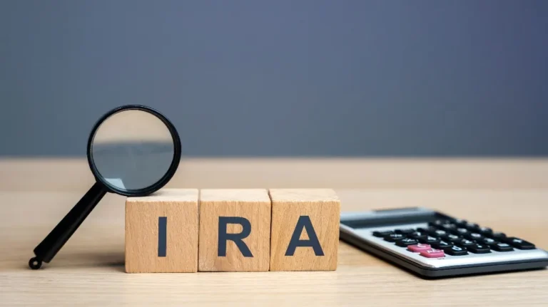 Magnifying glass, wooden blocks spelling "IRA," and calculator on wooden surface.