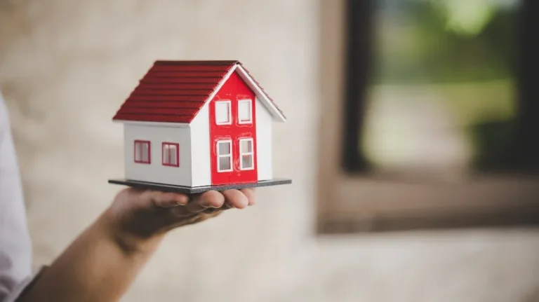 Hand holding a small white and red model house with a tiled roof.
