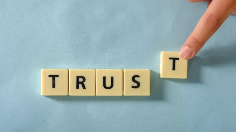 Hand placing the letter "T" tile to complete the word "TRUST" on a blue surface.