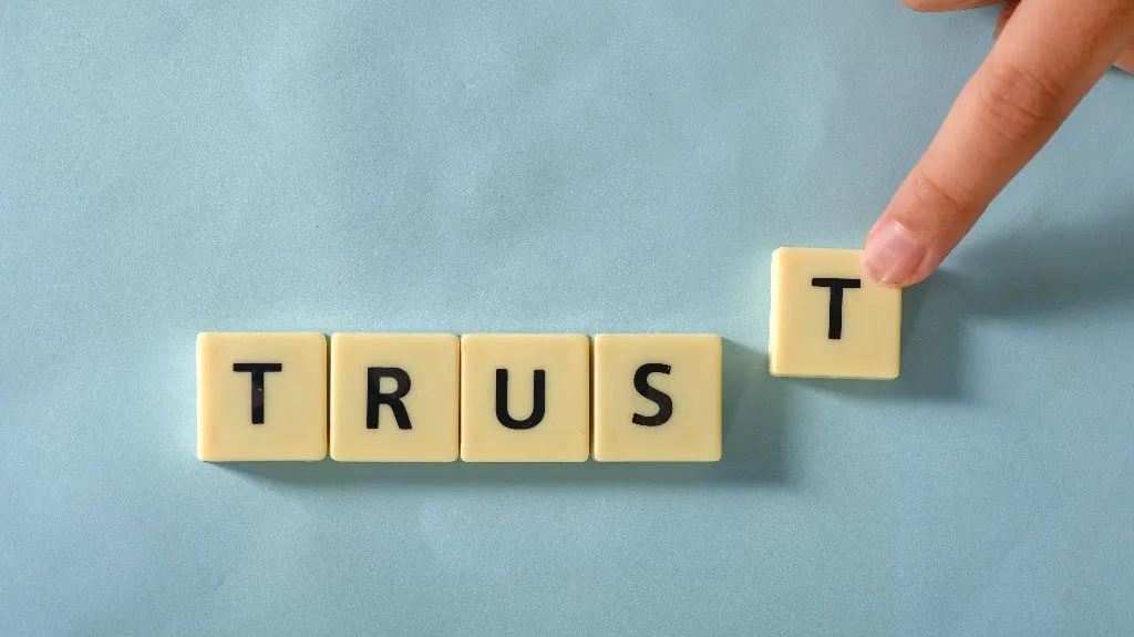 Hand placing the letter "T" tile to complete the word "TRUST" on a blue surface.