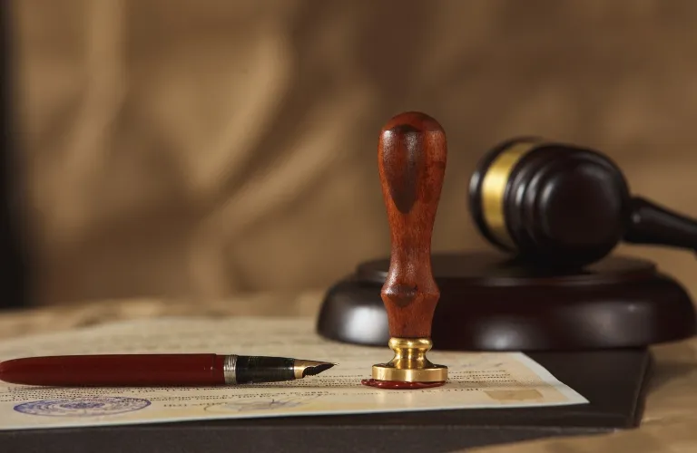 Wooden stamp with red wax seal, fountain pen, and gavel on legal document.