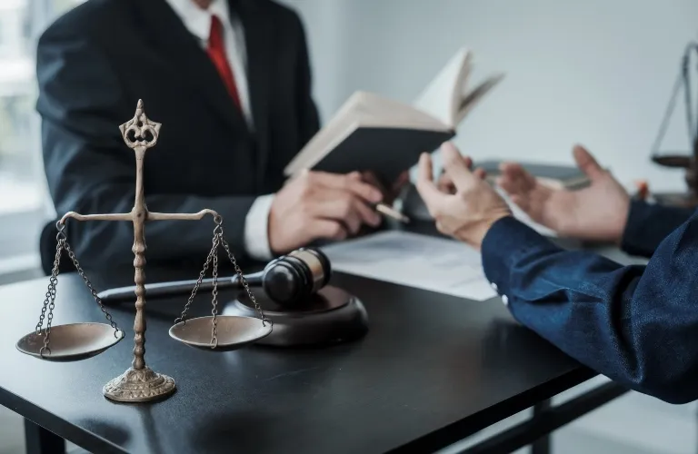 Two individuals in a legal consultation with scales of justice and gavel on black table.