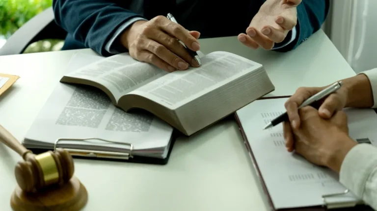 Two individuals reviewing legal documents with an open book, clipboard, and wooden gavel on a white table.