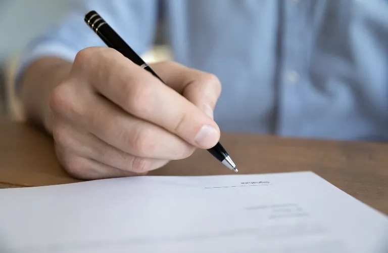 Close-up of a person holding a black pen poised to write on a document.